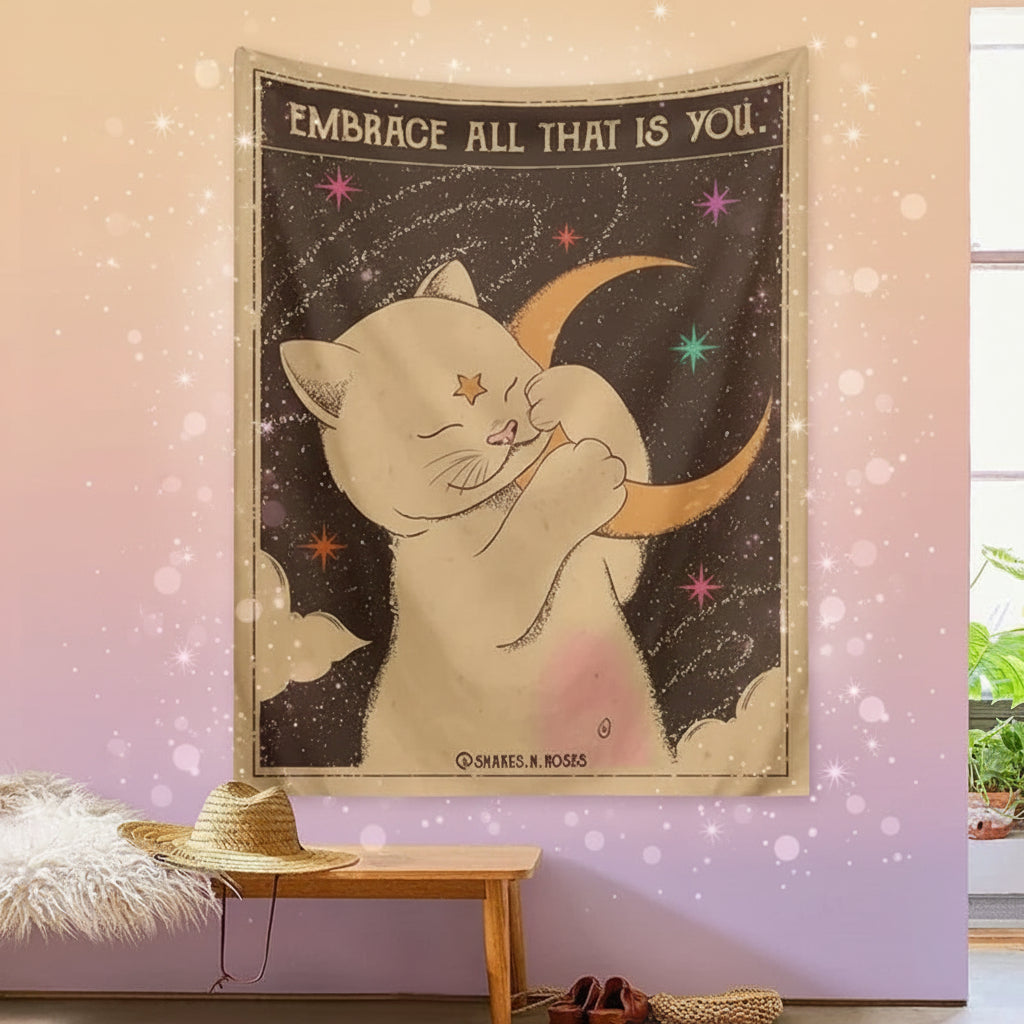 Tapestry with a cat holding a moon and stars, featuring the text 'Embrace All That Is You', hanging on a wall.
