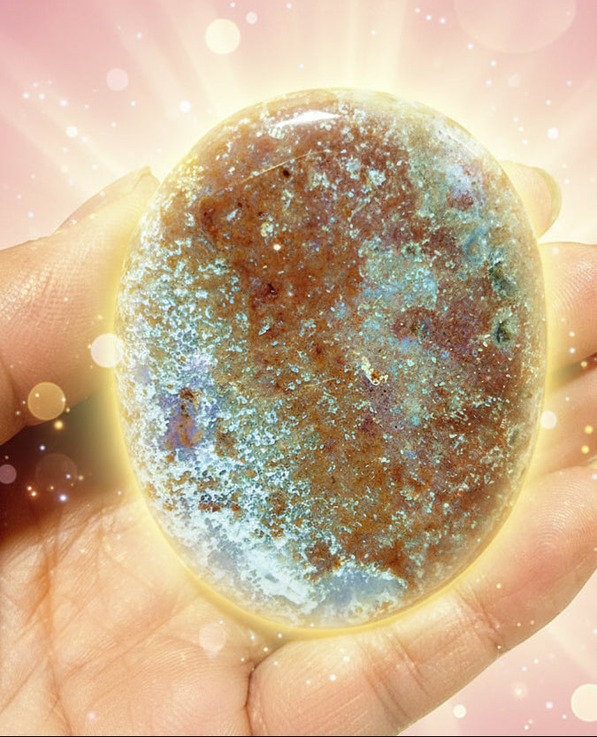 Round gemstone held in a hand with a green leafy background