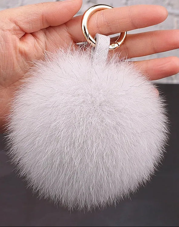 White fluffy keychain held by a hand against a neutral background
