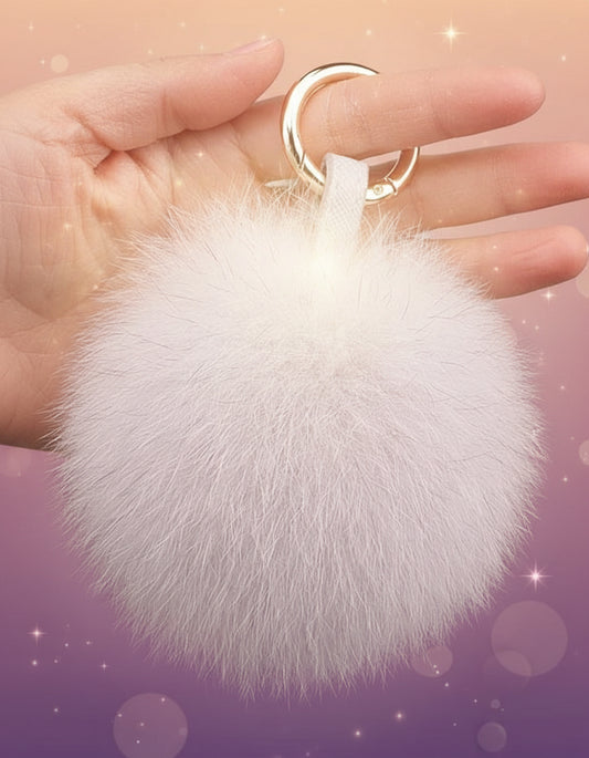 White fluffy keychain held by a hand against a neutral background