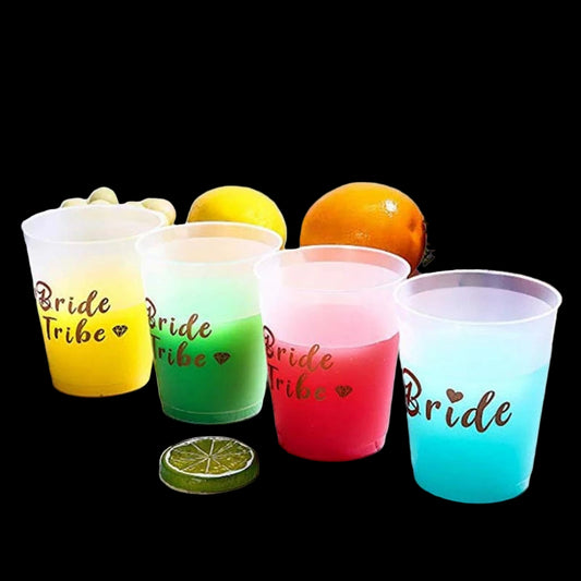 Colorful cups with 'Bride Tribe' and 'Bride' text on a wooden surface with fruits and flowers.