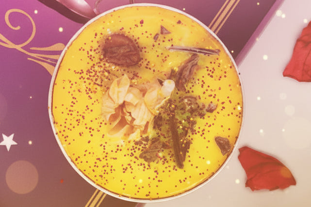 Yellow cocktail with garnishes on a decorative purple and gold menu with red rose petals.