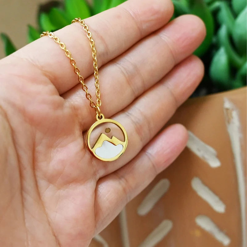 Gold necklace with a mountain pendant held in a hand against a blurred green background