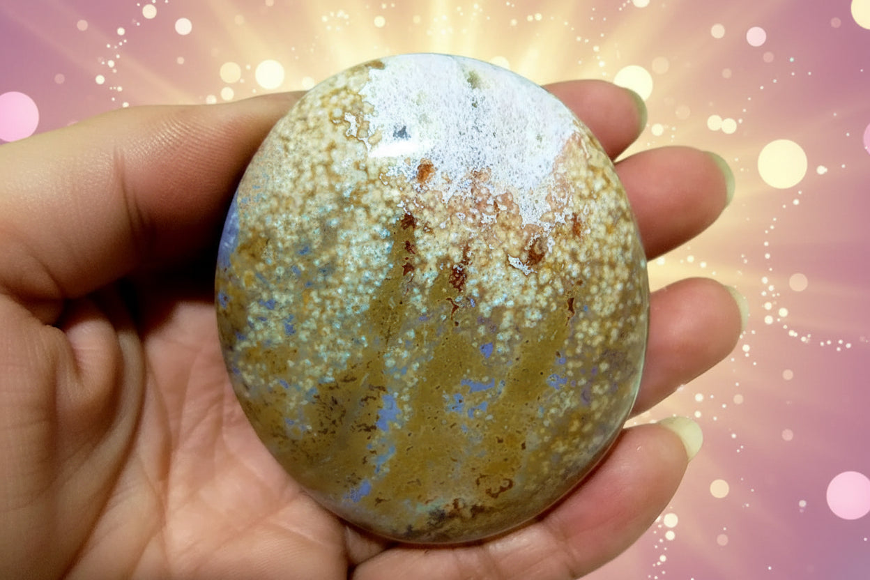 Round stone with marbled pattern held in a hand against a blurred green background