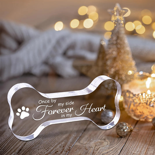 Decorative pet memorial plaque with text and paw print on a wooden surface with blurred lights in the background.