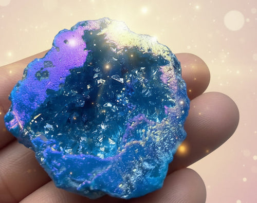 Blue geode crystal held in a hand with flowers in the background
