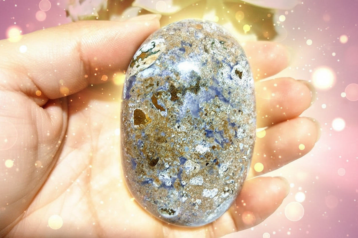 Hand holding a polished stone with a natural, multicolored pattern against a blurred green background
