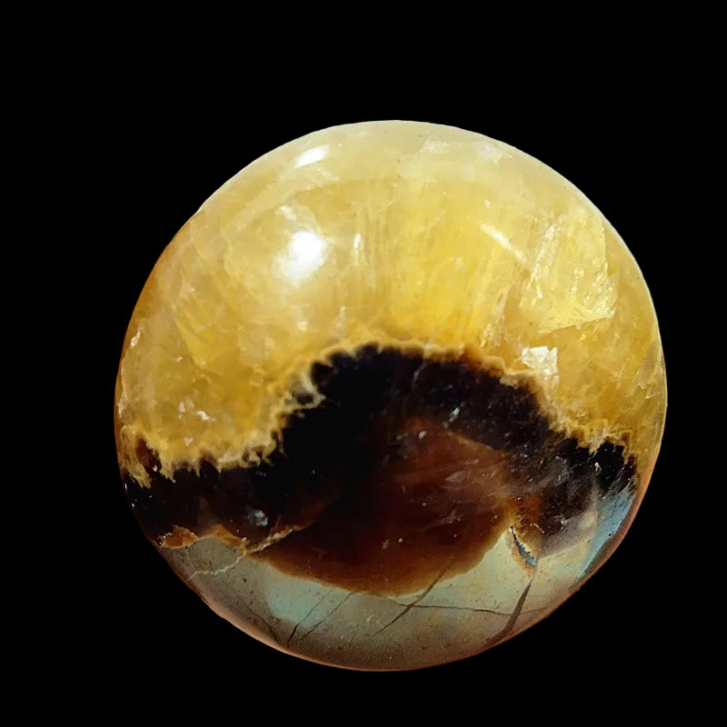 Hand holding a translucent yellow and brown crystal sphere against a blurred background