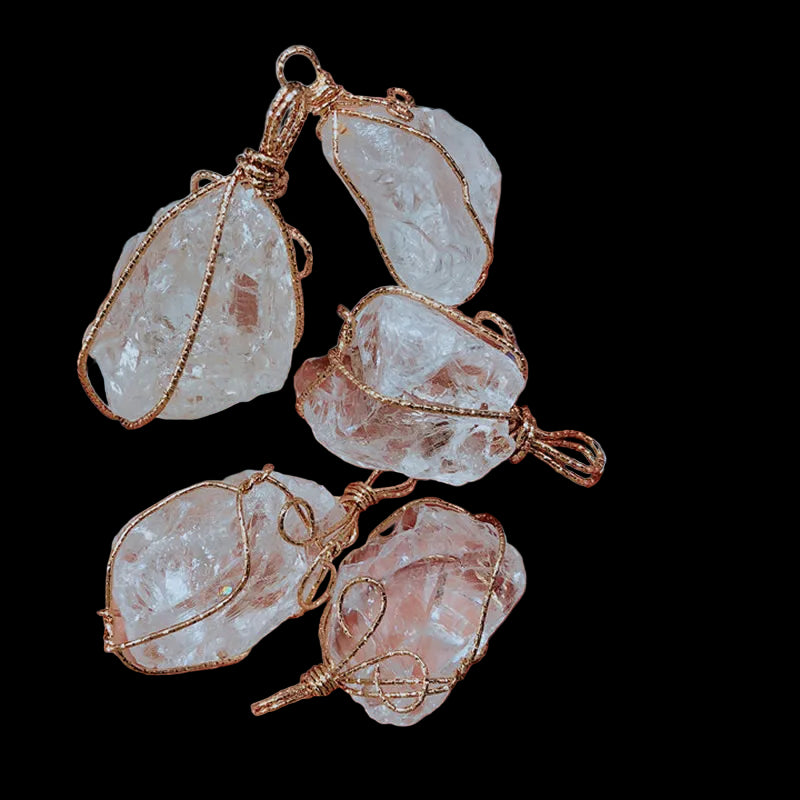 Clear crystal pendants with gold wire wrapping held in a hand against a blurred background