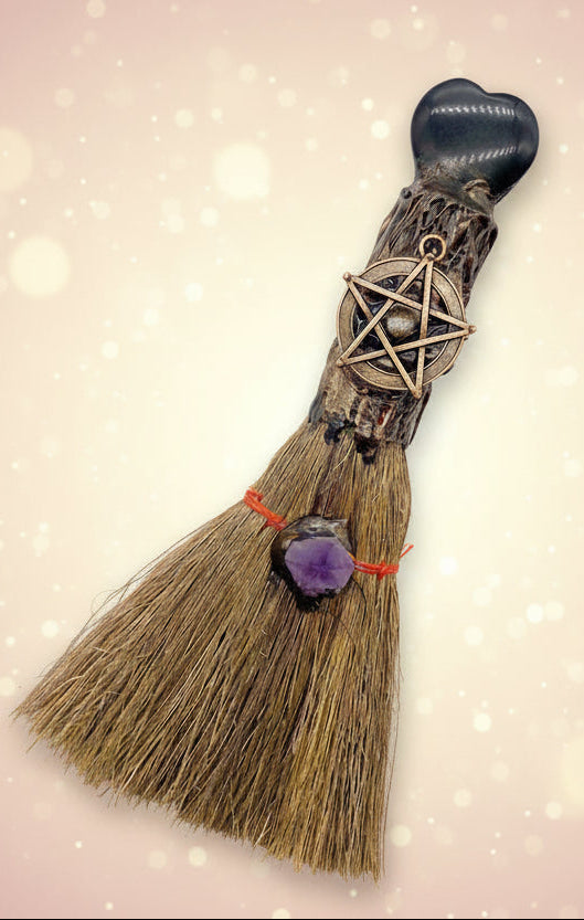 Decorative broom with pentacle charm and purple stone on a white background