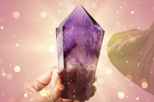 Amethyst crystal held in a hand with a green leaf in the background