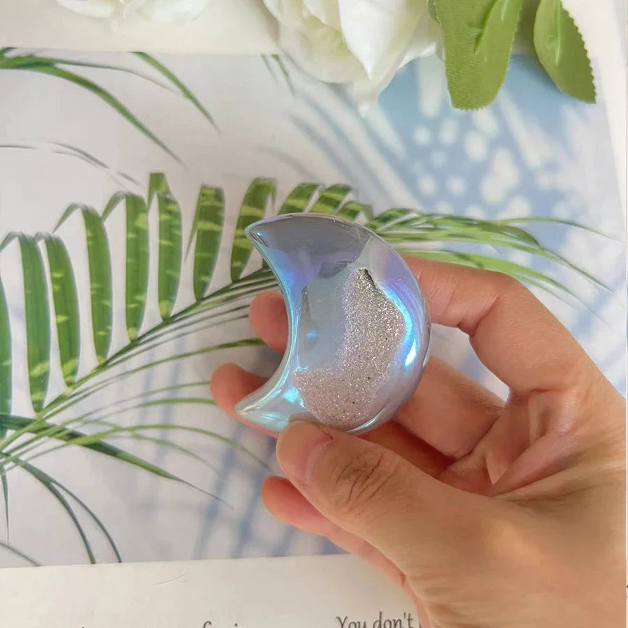 Hand holding a metallic crescent moon-shaped object with a floral and leafy background