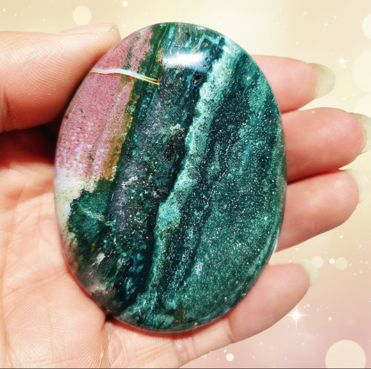 Multicolored gemstone held in a hand with a blurred natural background