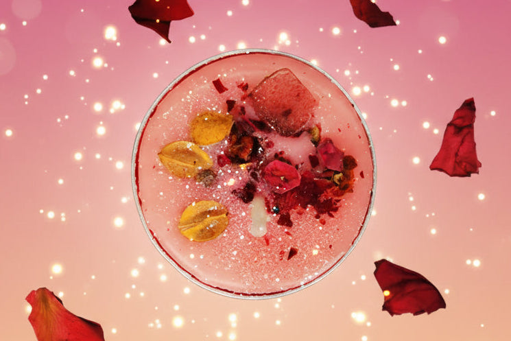 Pink cocktail with fruit pieces on a purple surface with rose petals