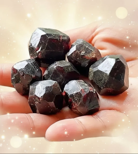 Hand holding dark red garnet crystals with a background of more garnets.