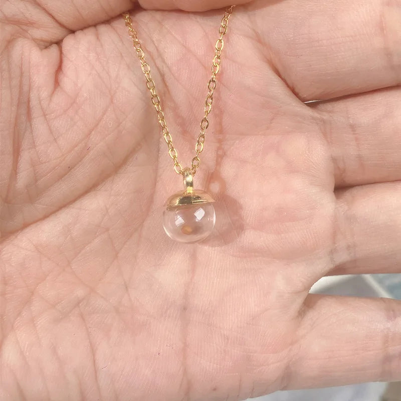 Gold necklace with a clear pendant held in a hand