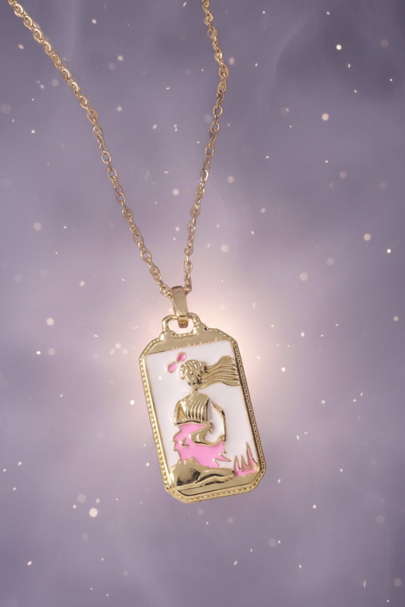 Gold necklace with a mermaid pendant on a textured beige surface