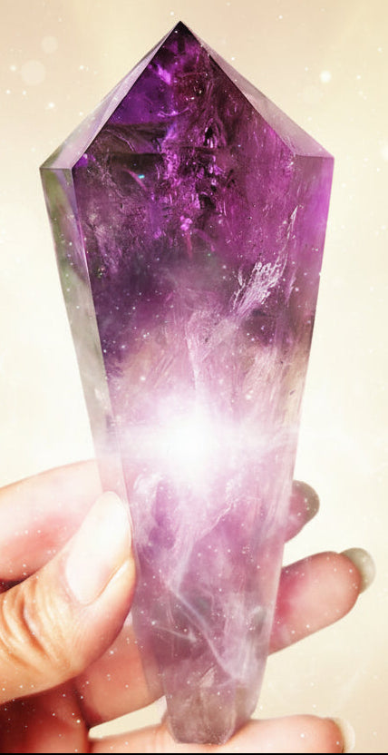 Amethyst crystal held in a hand with green leaves in the background