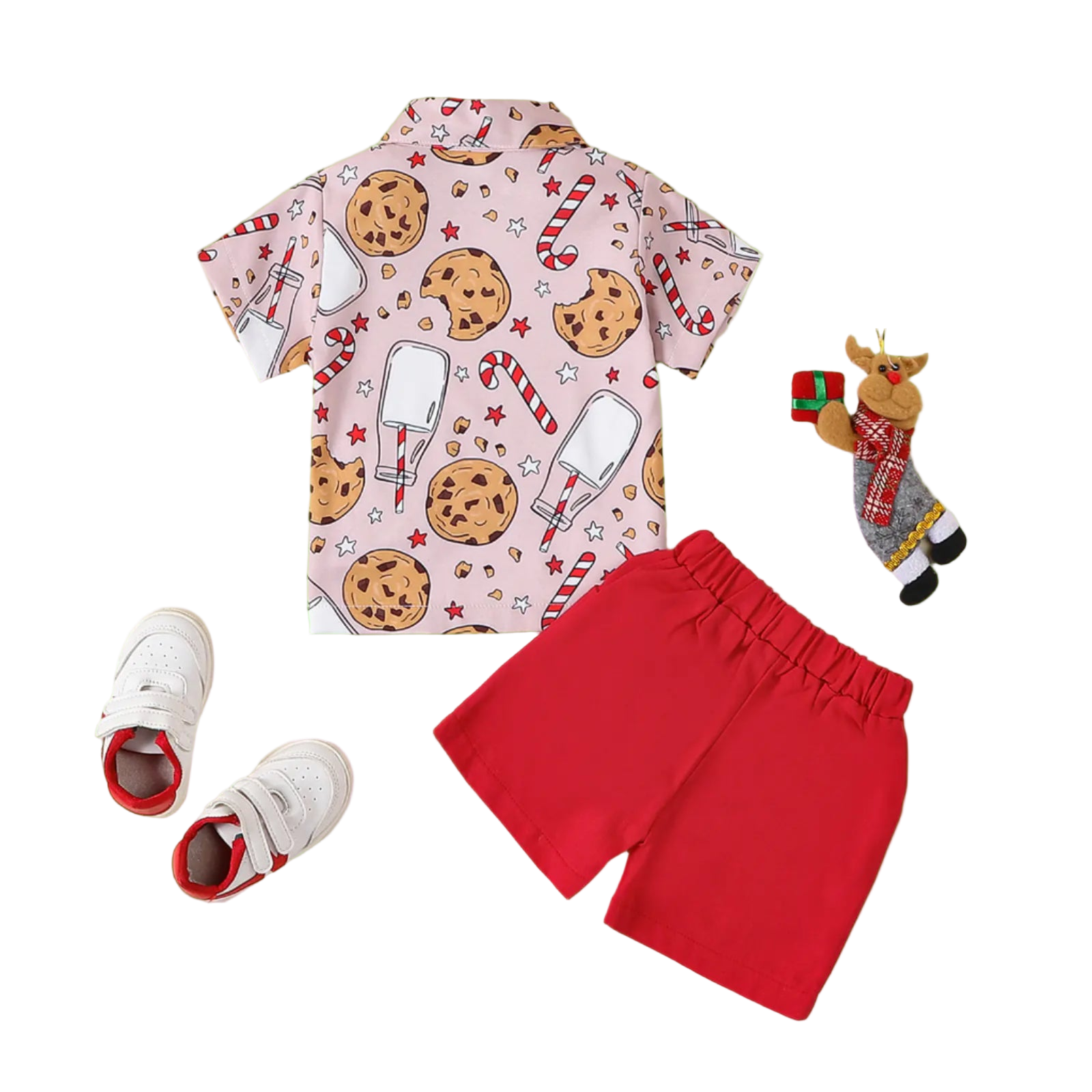 Children's outfit with a pink shirt featuring cookies and candy, red shorts, white sneakers, and Christmas-themed accessories on a beige background.