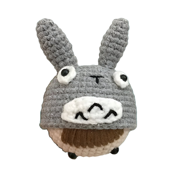 Hand holding a small crochet toy resembling a character with gray ears and white face on a green background