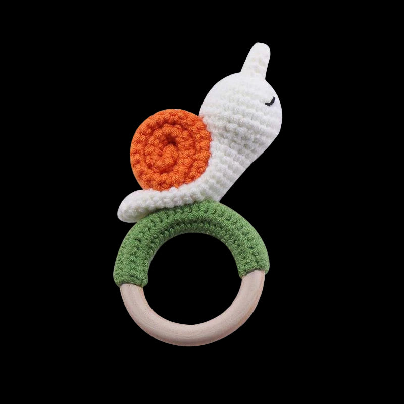 Crocheted toy with a white snake-like figure, orange circle, green ring, and wooden ring on a white background