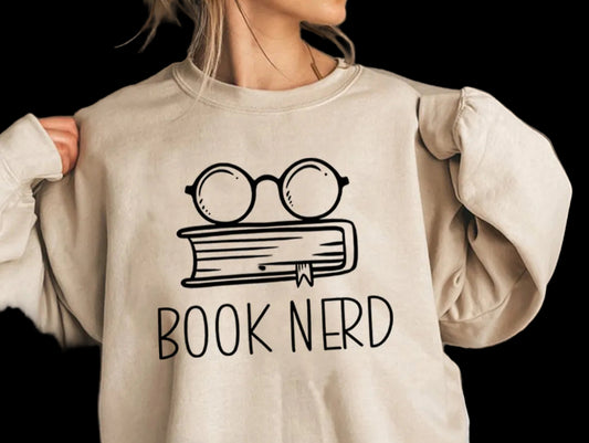 Person wearing a beige sweatshirt with 'Book Nerd' design and glasses on a book.