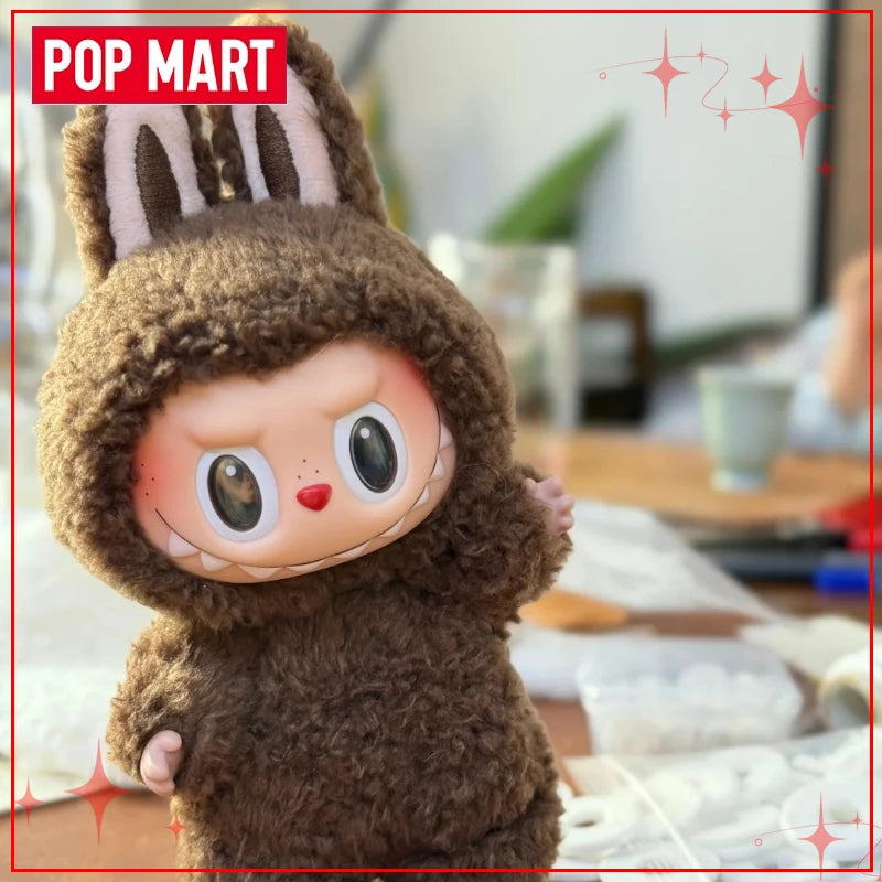 Toy figure in a brown outfit with a hood, resembling a bear, on a blurred indoor background with 'Pop Mart' branding.