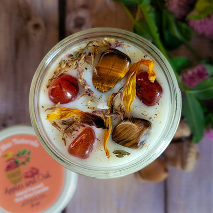 Top-down view of a glass jar candle filled with white wax and dried botanicals, including tiger's eye, red berries, and yellow flower petals, with a partial jar lid visible at the bottom left on a rustic wooden surface.