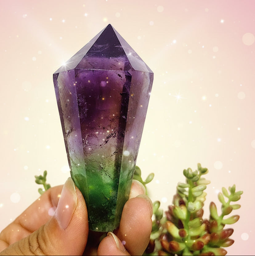 Hand holding a faceted purple crystal with a green plant in the background