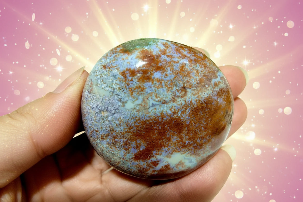 Round stone with brown and blue speckled pattern held in a hand against a blurred green background