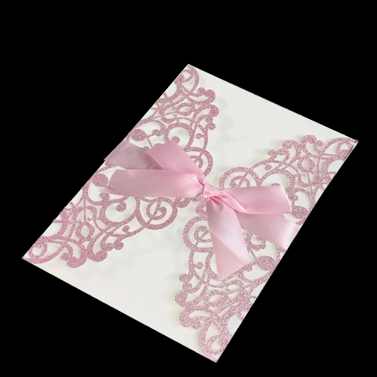Lace invitation card with a pink ribbon on a dark textured surface