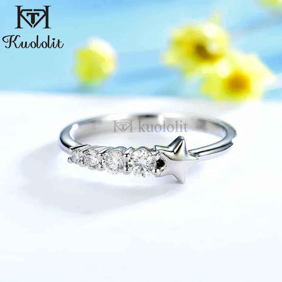 Silver ring with three diamonds on a white surface with blurred yellow flowers in the background, featuring the brand 'Kuololit'.