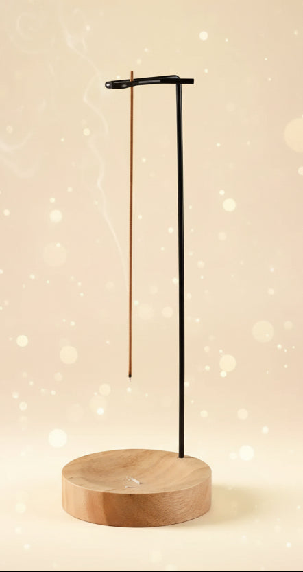 Incense burner with two incense sticks on a wooden base, emitting smoke against a warm background.