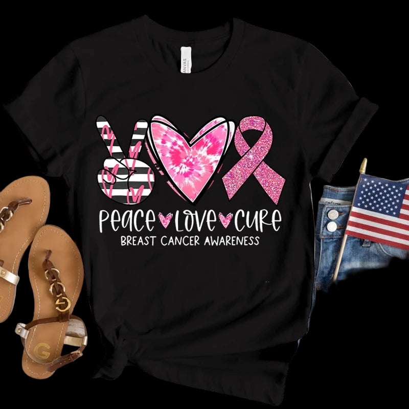 Black t-shirt with pink breast cancer awareness design on a wooden surface with sandals and an American flag.