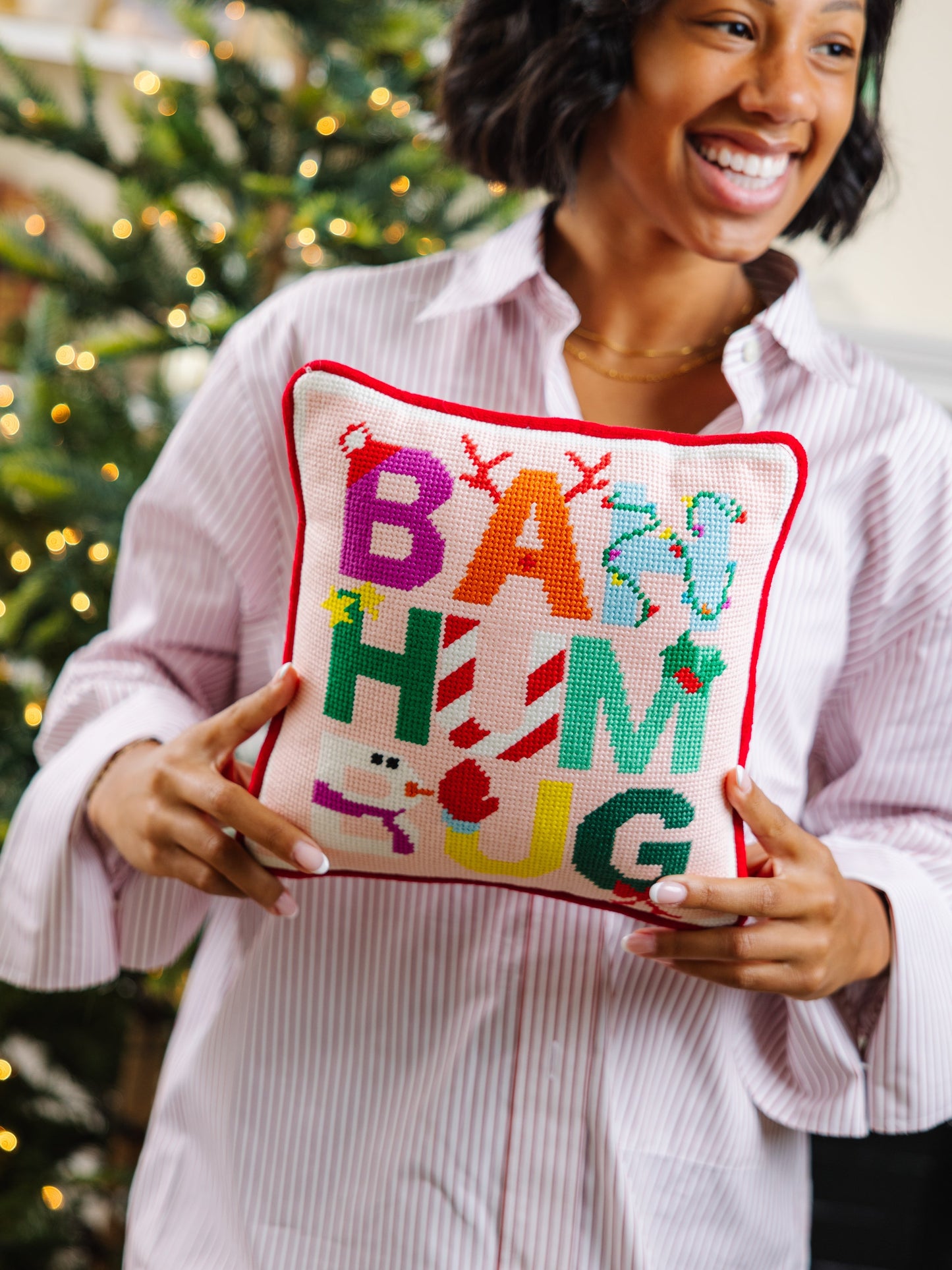 Person holding a colorful pillow with 'BAH HUM HUG' text in front of a Christmas tree.