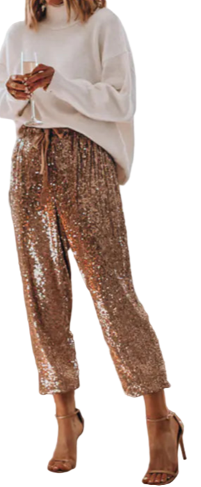 Woman in a living room wearing a white sweater and gold sequin pants, with a Christmas tree in the background.