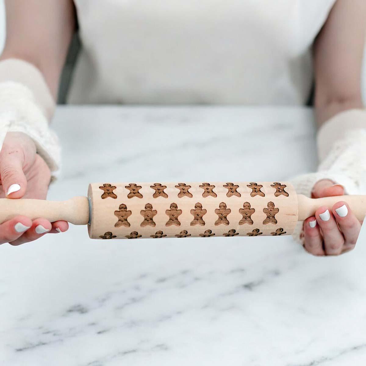 Person holding a wooden rolling pin with gingerbread man design on a marble surface