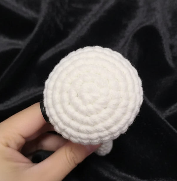 White knitted dog toy held by a hand on a gray background