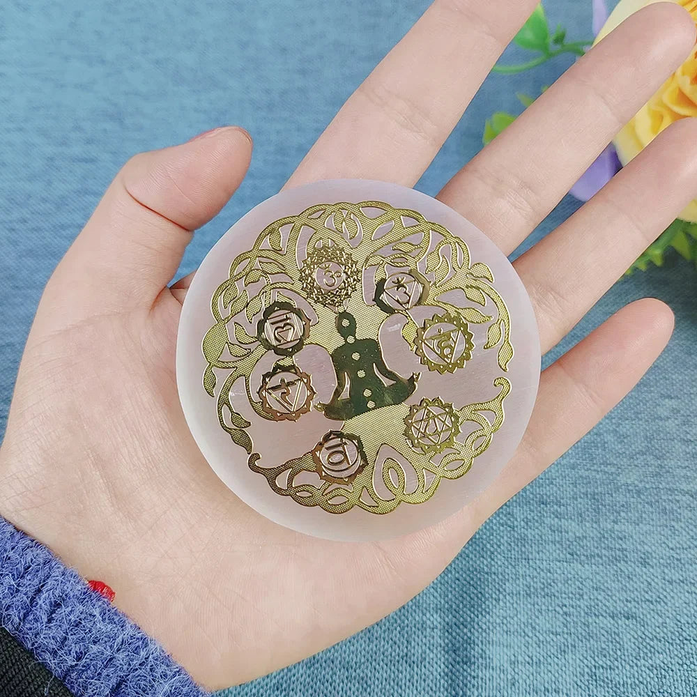 A hand holding a round translucent silicone mold or coaster featuring a gold foil design of a figure meditating within a floral and knot pattern, set against a blue textured background.