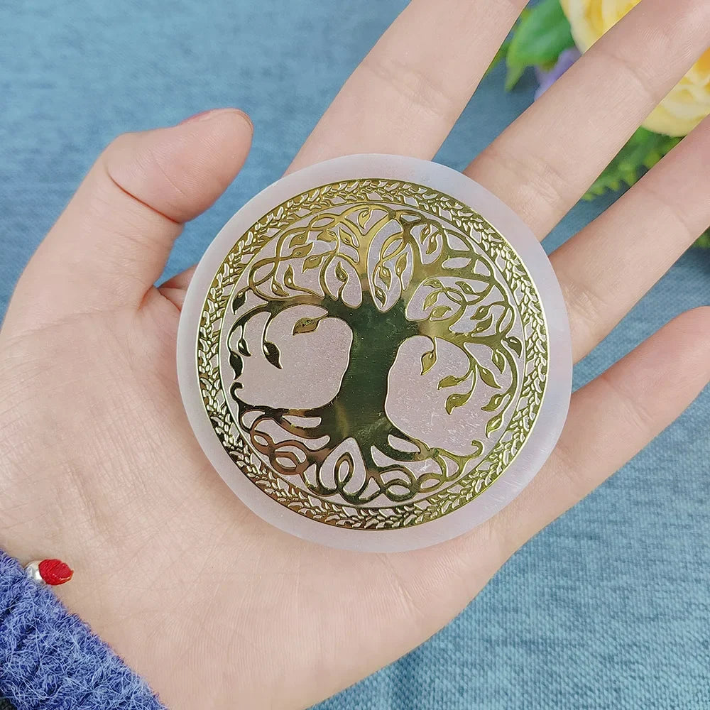 Decorative circular object with tree design held in a hand against a blue background
