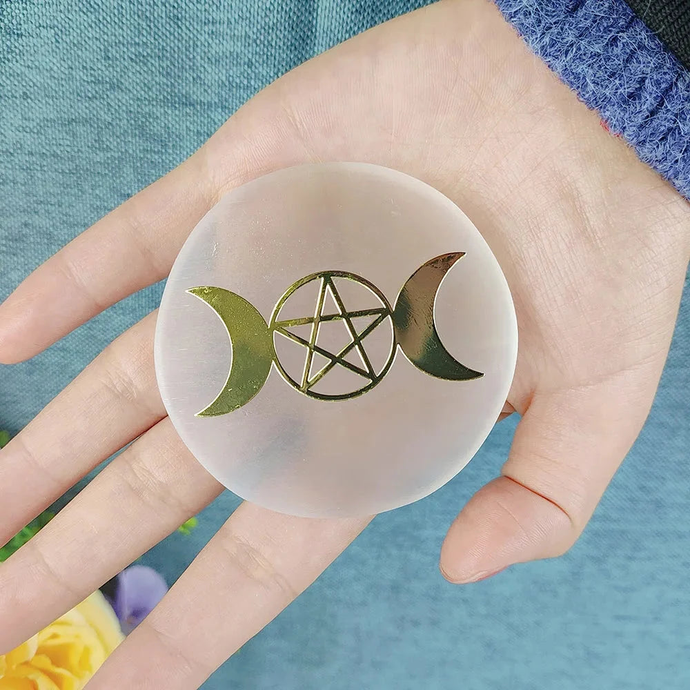Hand holding a round, translucent object with gold pentagram and moon designs against a blue background.