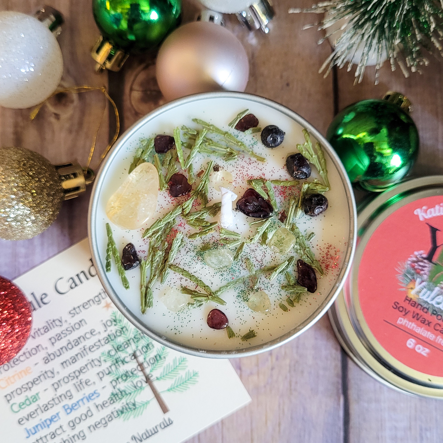 Candle with herbs and spices surrounded by Christmas ornaments on a wooden surface