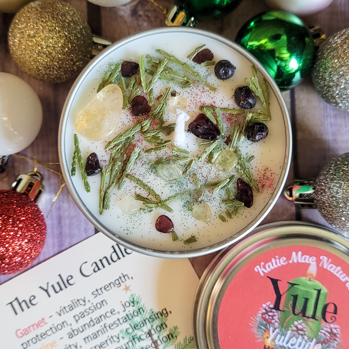 Candle with decorative elements and 'Katie Mae Naturals' branding on a festive background.
