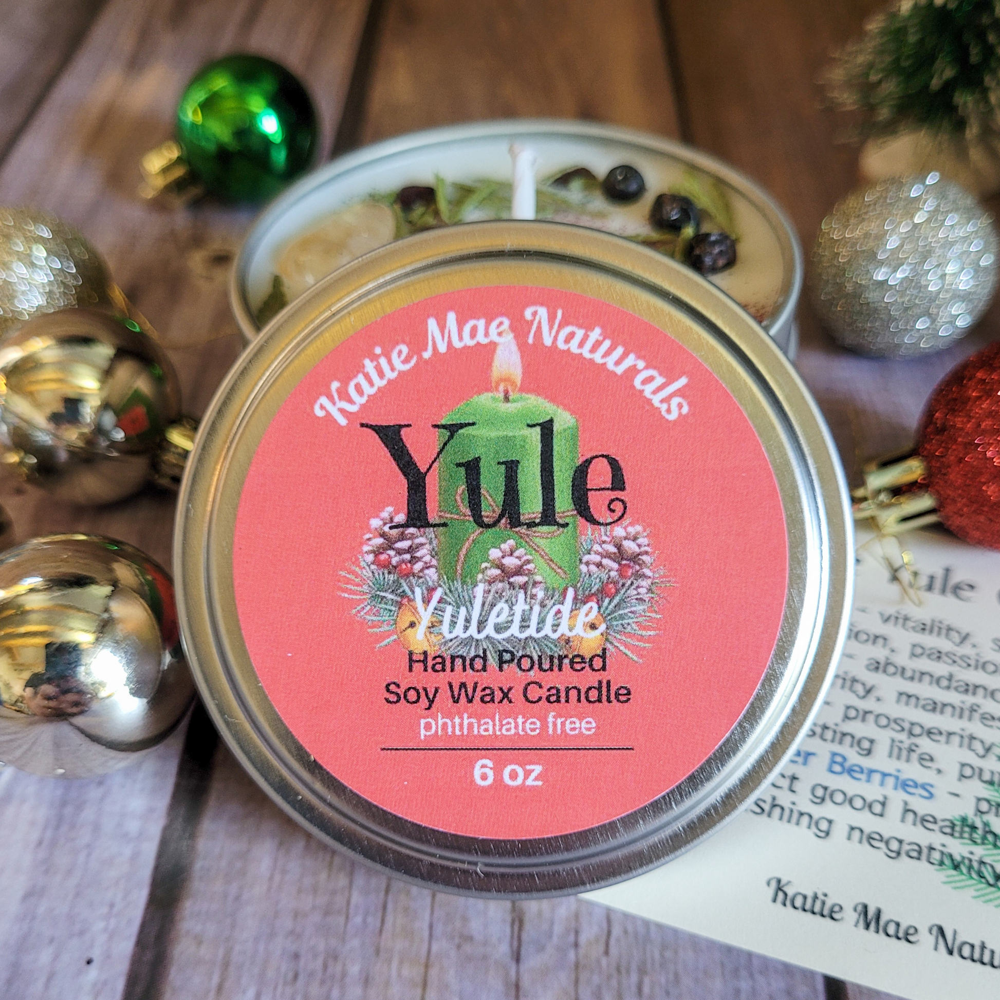 Katie Mae Naturals Yule candle with decorative Christmas ornaments on a wooden surface