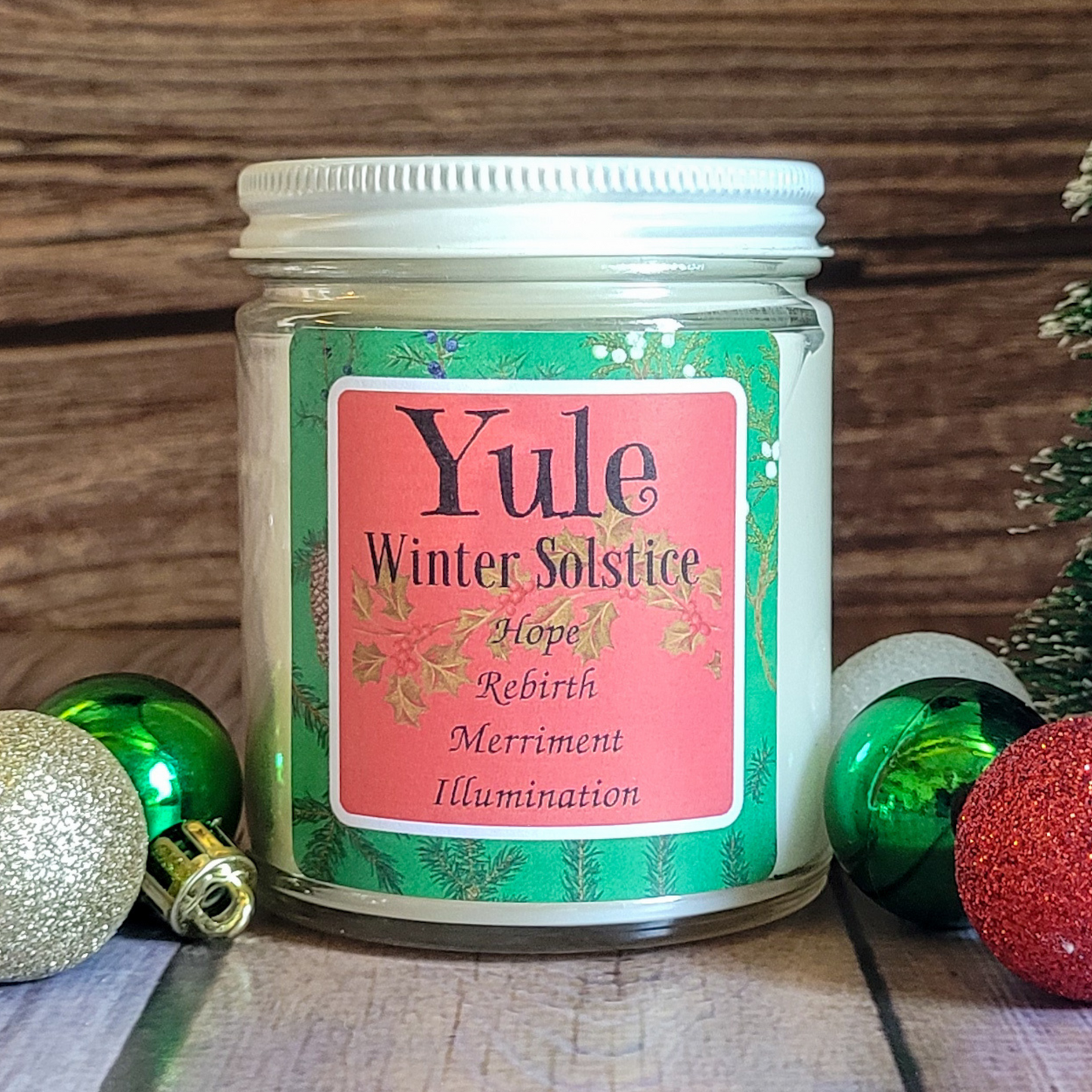Candle jar labeled 'Yule Winter Solstice' with decorative Christmas ornaments on a wooden surface.