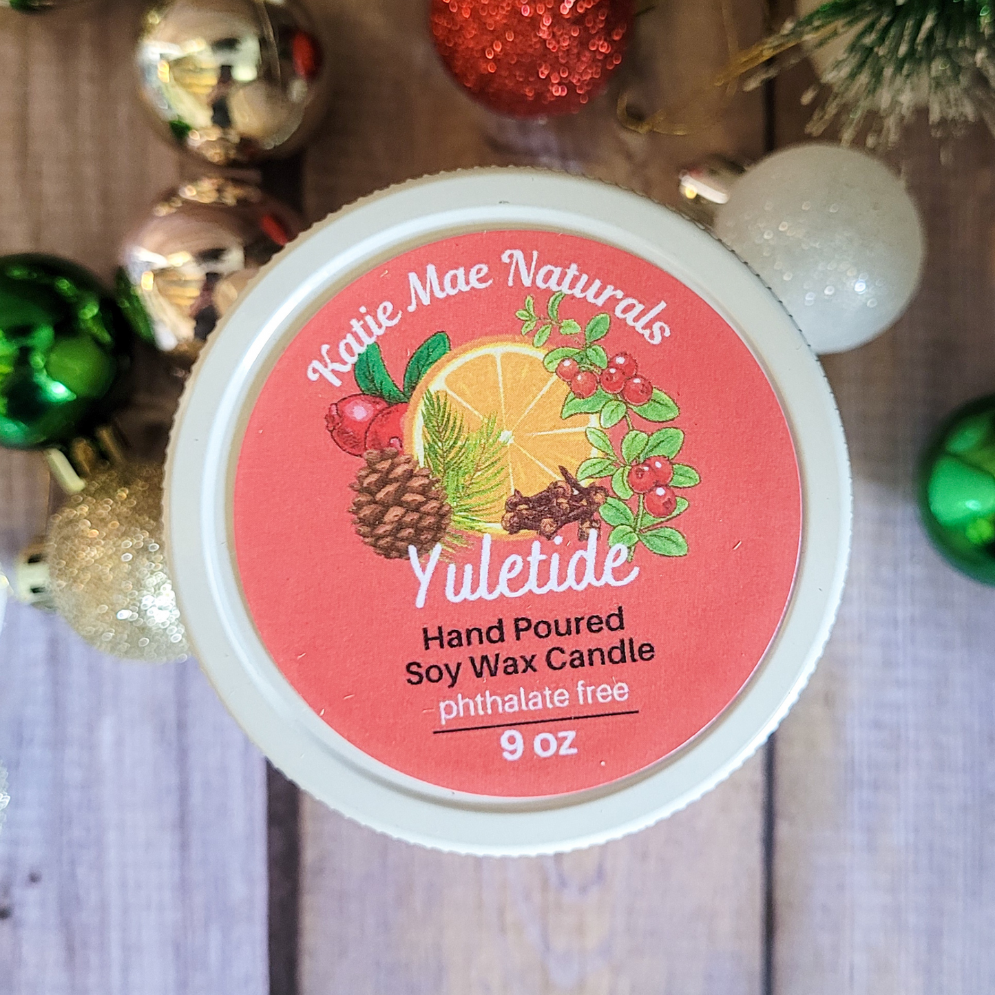 Katie Mae Naturals Yuletide candle with decorative ornaments in the background