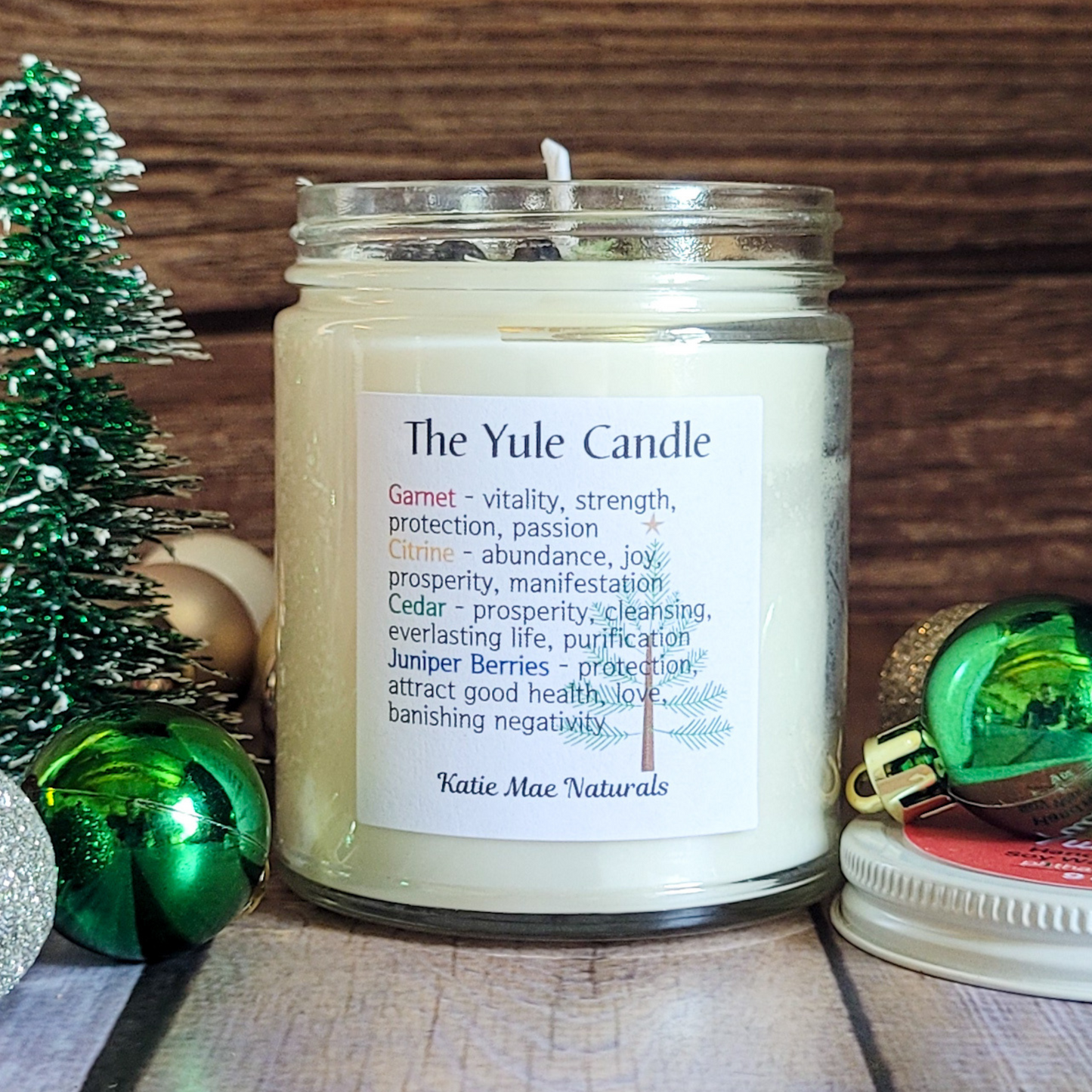 Candle labeled 'The Yule Candle' with a decorative Christmas tree and ornaments on a wooden surface.