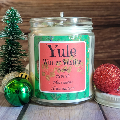 Candle jar labeled 'Yule Winter Solstice' with decorative Christmas ornaments on a wooden surface.