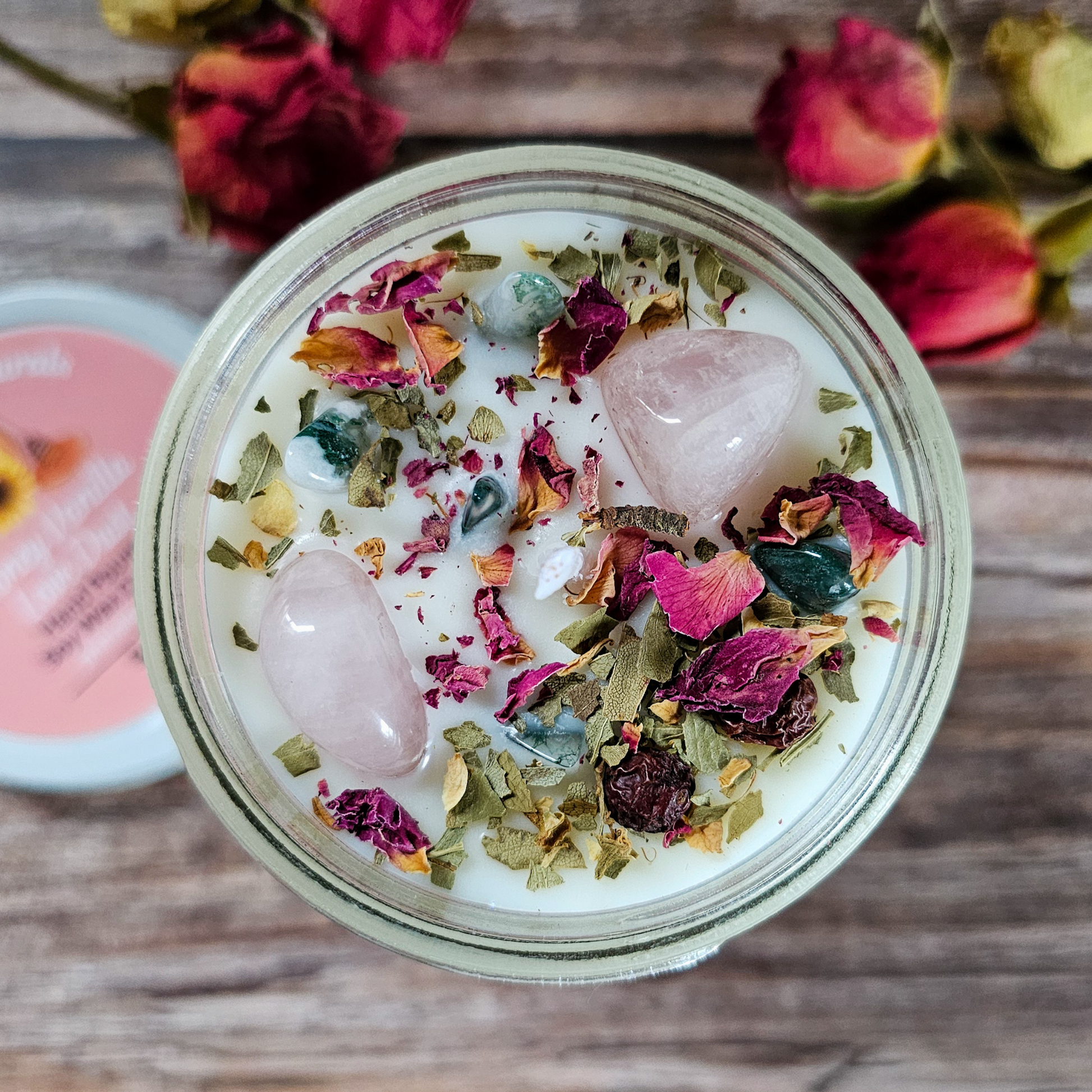 Jar with pink stones, dried flowers, and herbs on a wooden surface