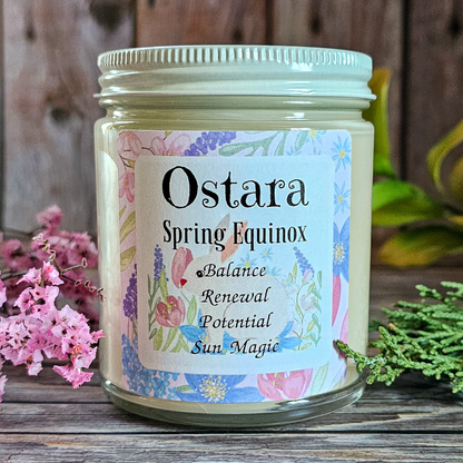 Candle jar labeled 'Ostara Spring Equinox' with floral design on a wooden surface.